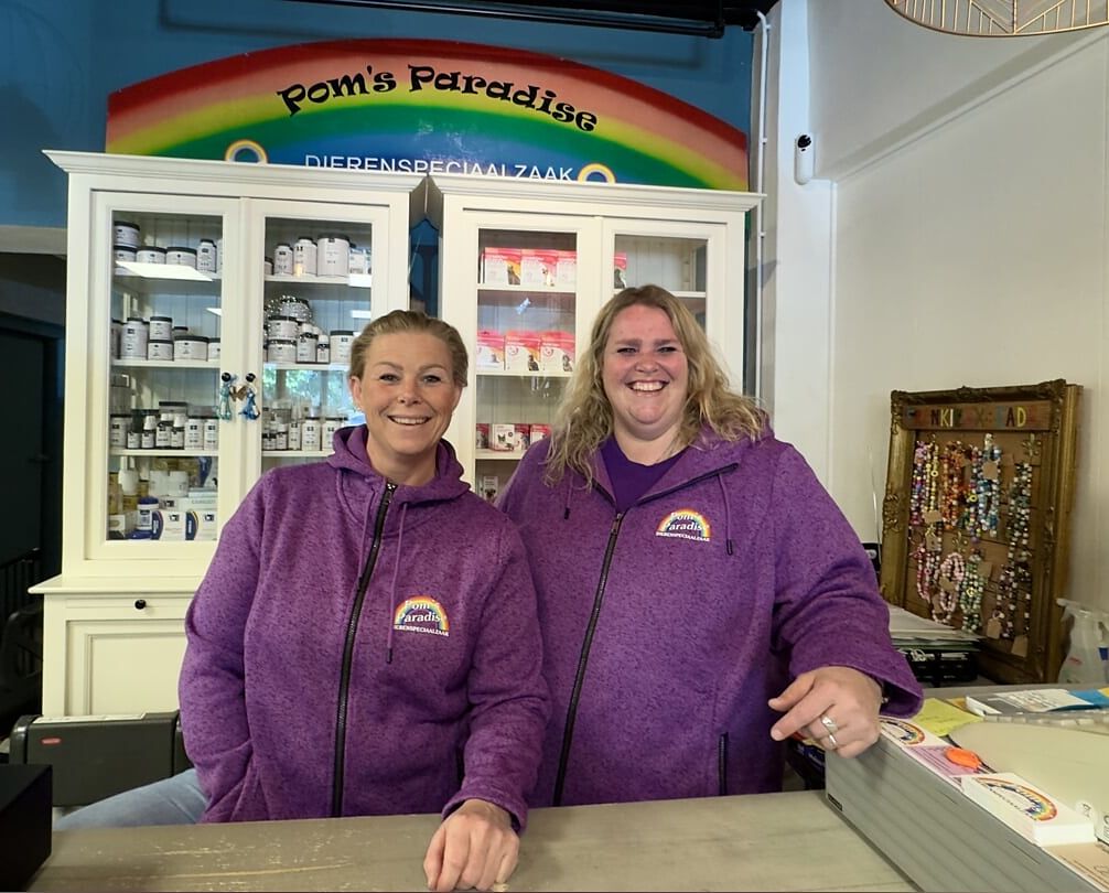 Twee medewerkers van Pom's Paradise in paarse vesten achter de toonbank, onder het regenboogbord van de winkel